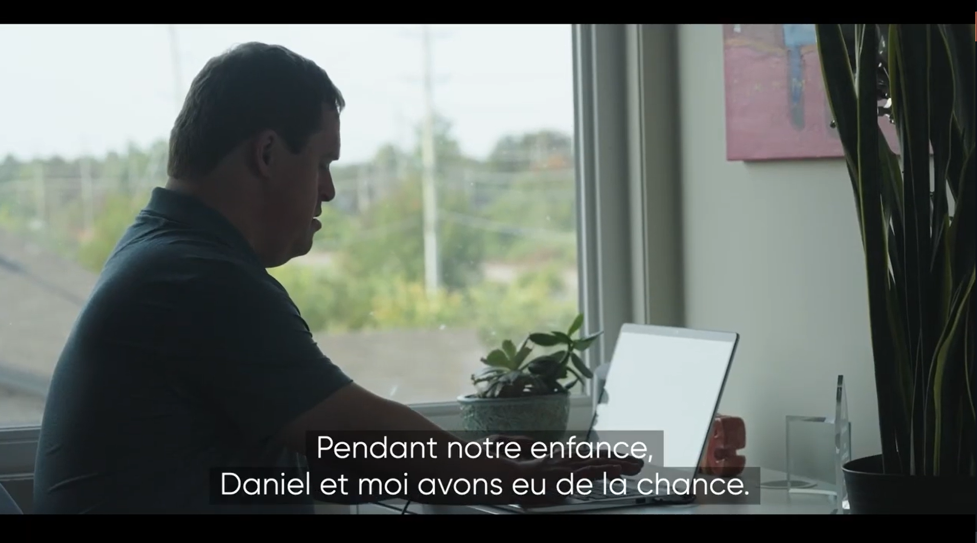 Capture d'écran de la minute 02:20 de la vidéo montrant Daniel s’assoire devant son ordinateur portatif et tape au clavier. La caméra s’arrête sur un portrait de famille. Daniel prend la photo et la regarde.