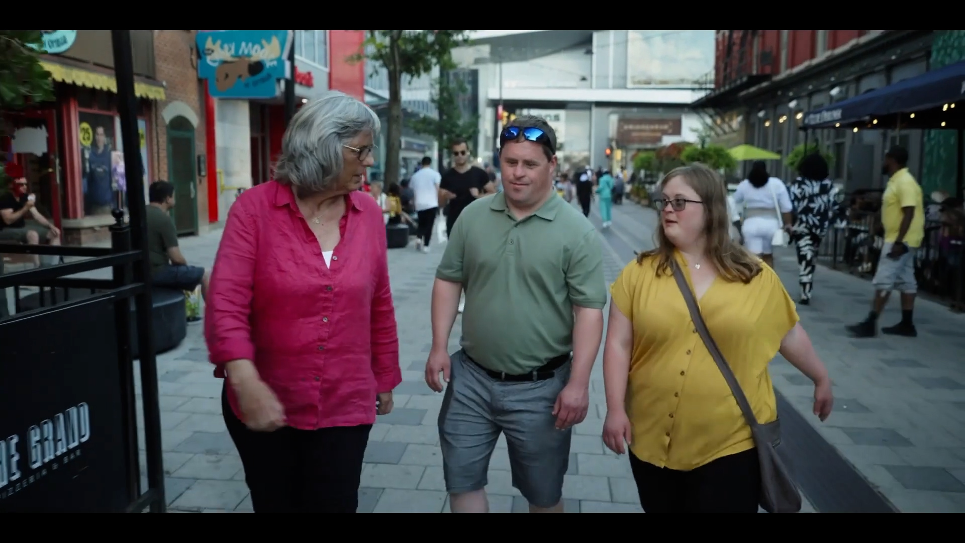 Capture d'écran de la minute 01:53 de la vidéo montrant Daniel et Lisa sortir de la station de train léger et marchent dans la rue pour accueillir Kathy.