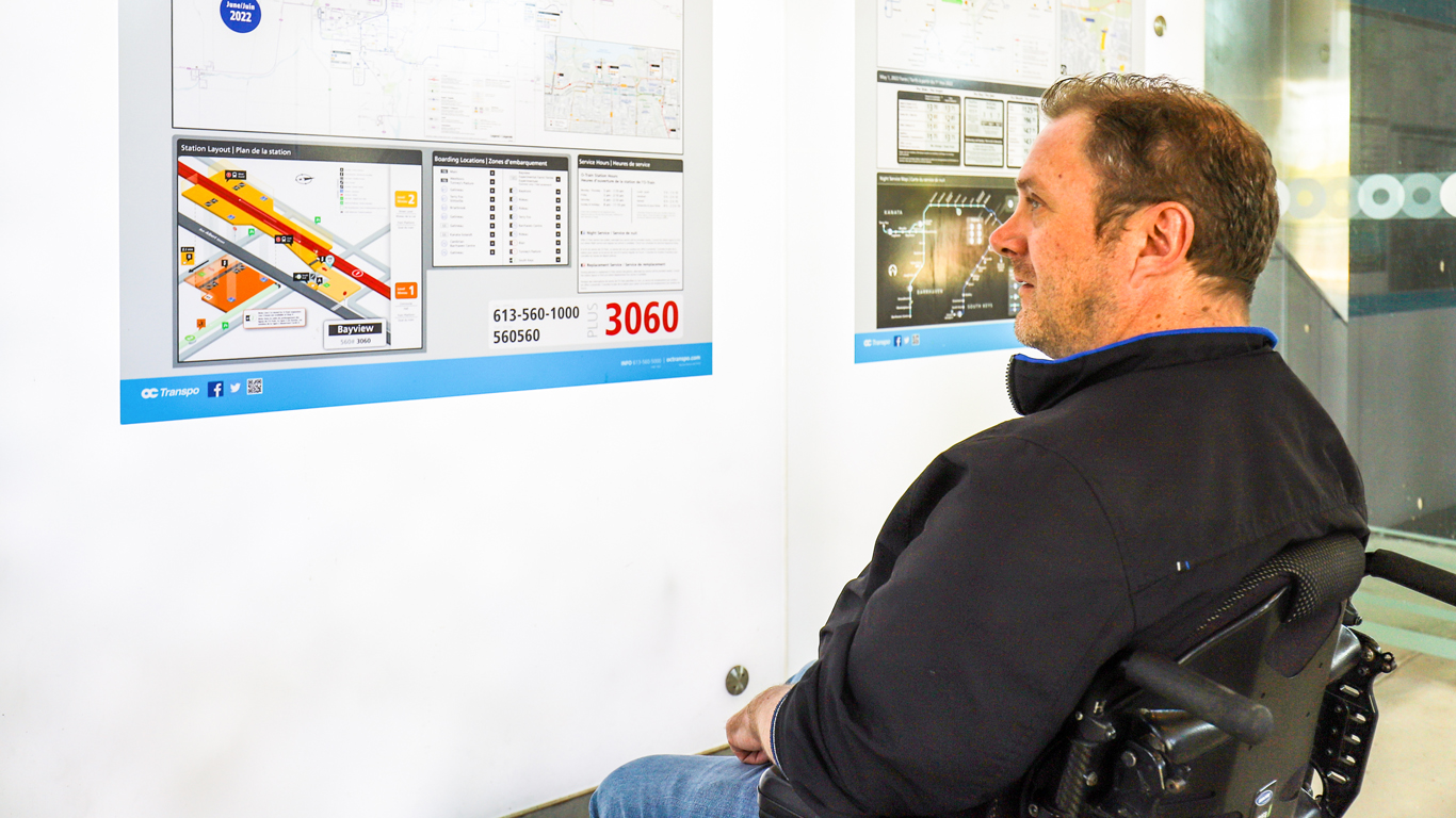  Usager en fauteuil roulant observant le plan d'orientation à la station de l'O-train